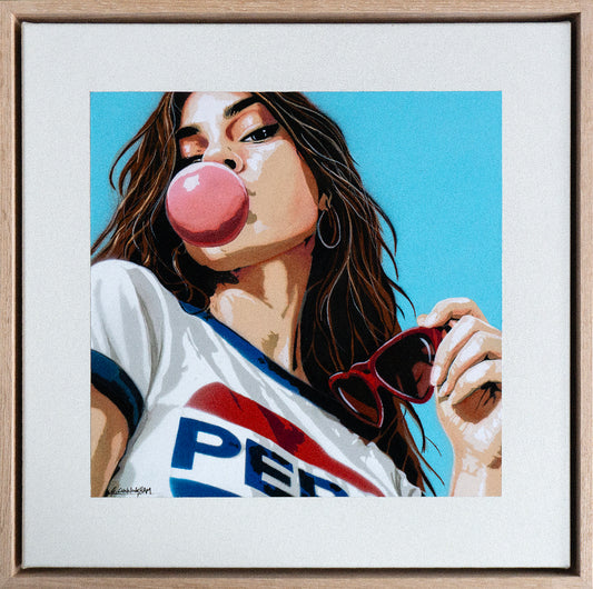 Framed artwork of a woman blowing a bubble with bubble gum, wearing a Pepsi shirt.