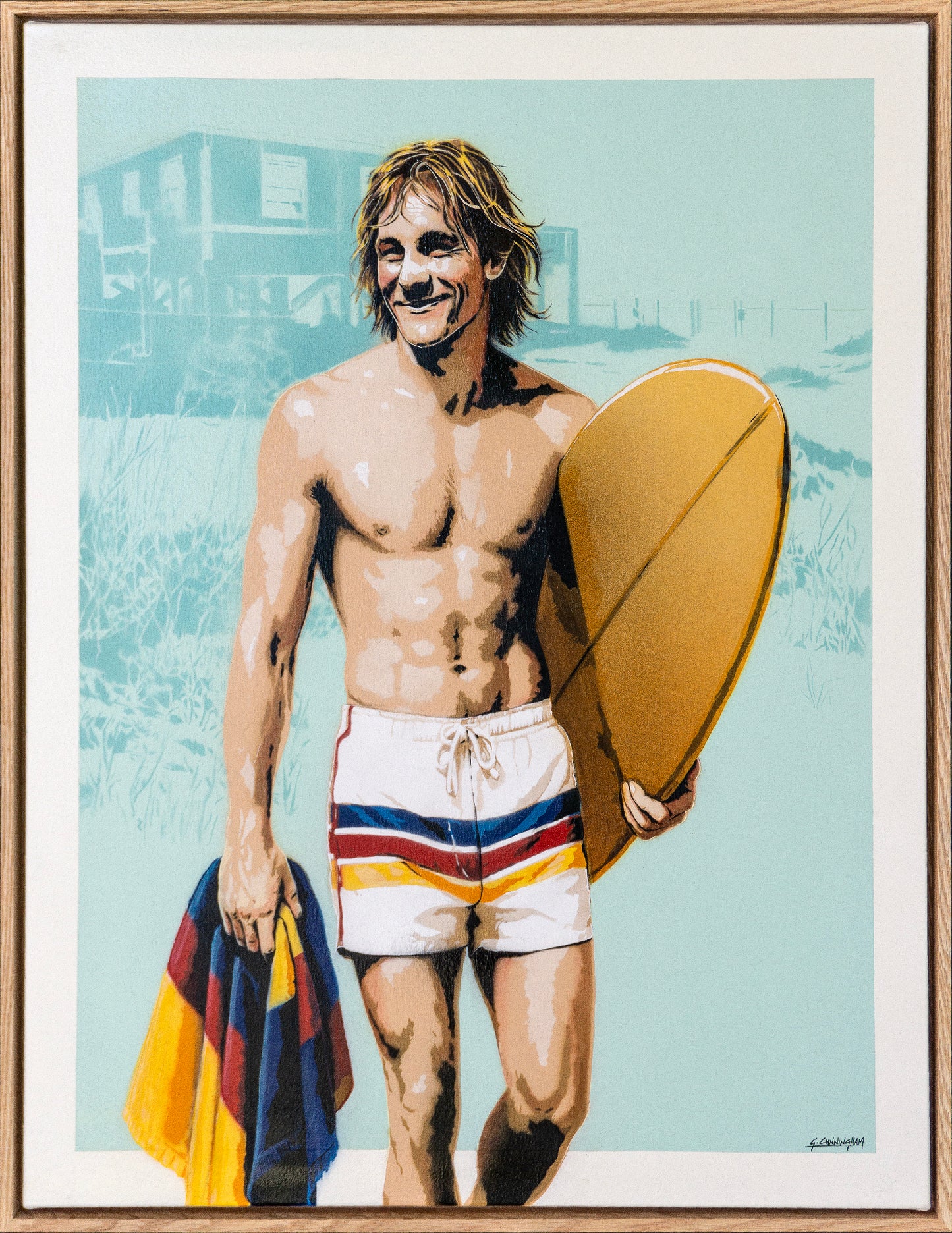 a male surfer walks along a beach with a surf club in the background