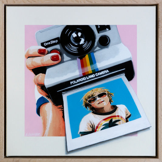 Framed artwork of a Polaroid camera and a person holding it with a colorful photo attached.