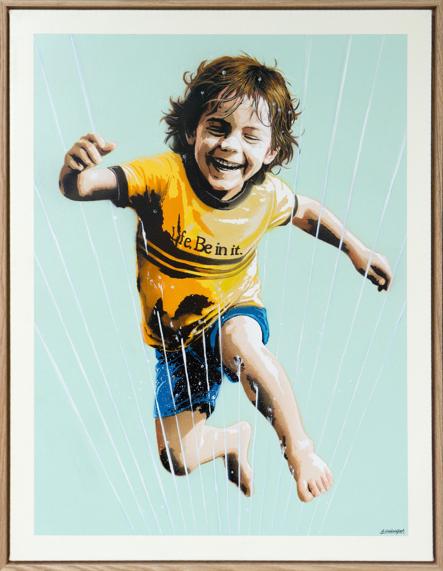 Framed artwork of a child in a yellow shirt with text, jleaping through a sprinkler with a light blue background.