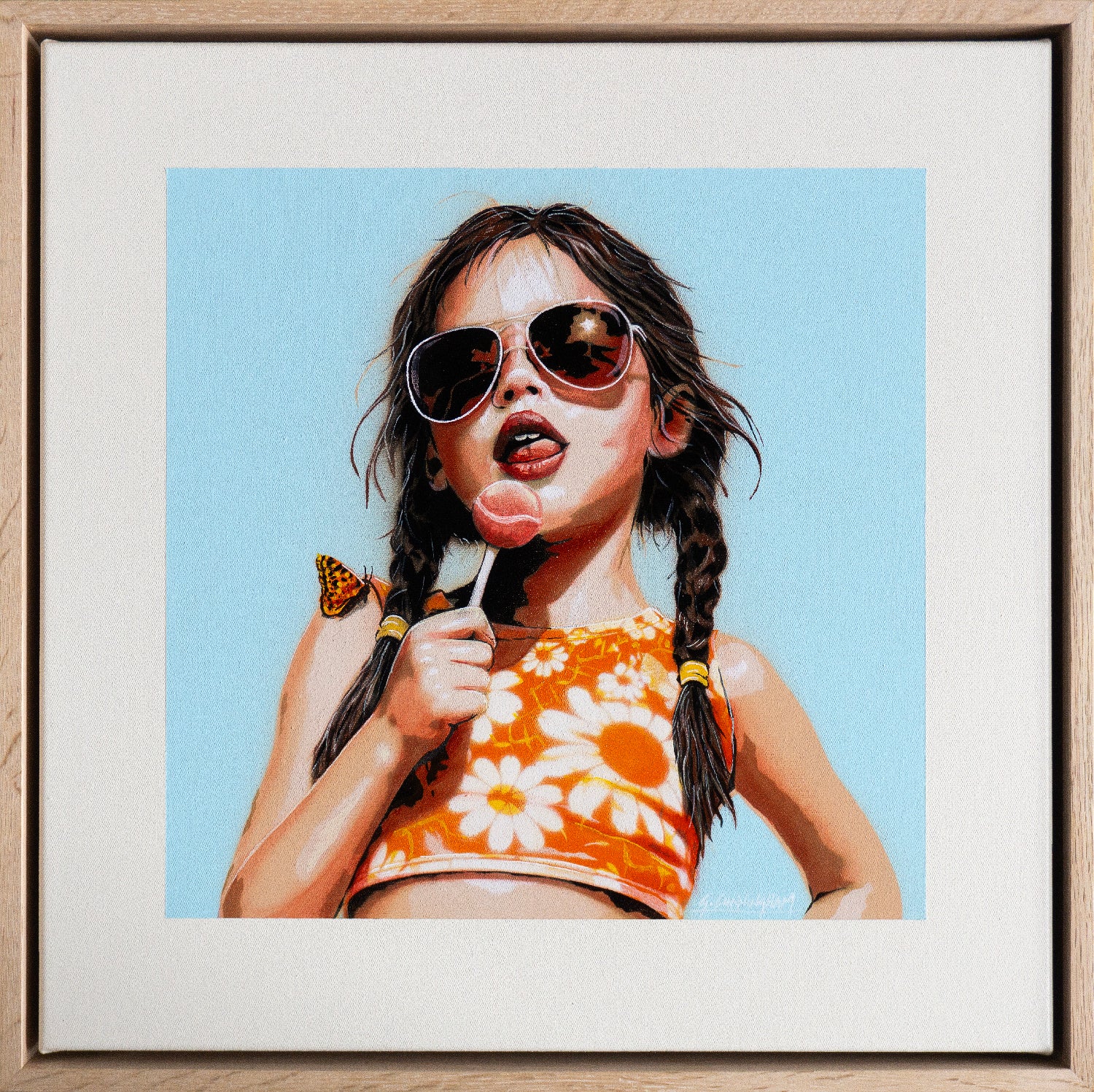 Framed artwork of a young girl with sunglasses, a lolly pop and a floral top against a blue sky.