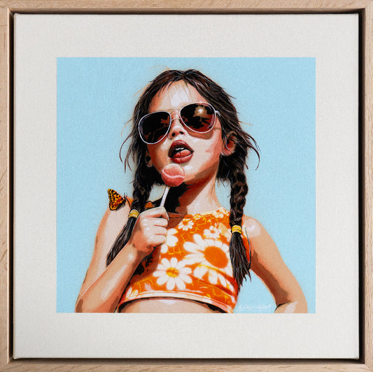 Framed artwork of a young girl with sunglasses, a lolly pop and a floral top against a blue sky.